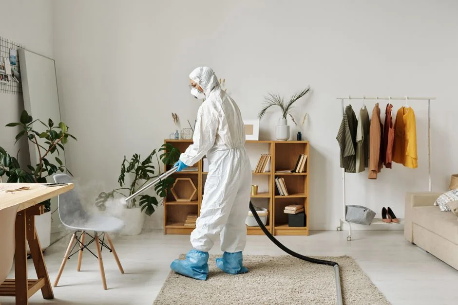 services-03 A professional cleaner in protective gear vacuuming the floor in a modern living room.